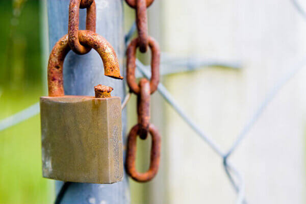 Cut rusty padlock, indicating weak security. Shallow depth of field with focus on cut in padlock.